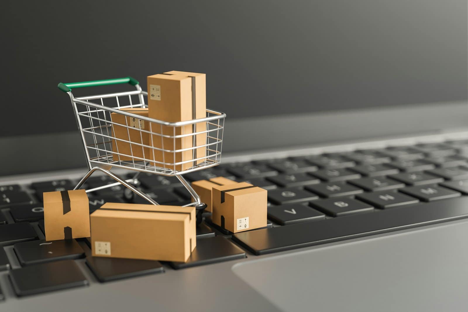 A small shopping cart on top of a computer keyboard, with shopping boxes around it