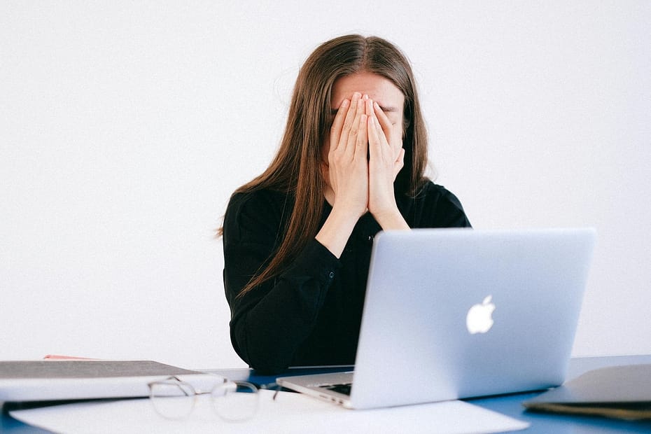 Woman in front of a laptop, with her hands covering her face